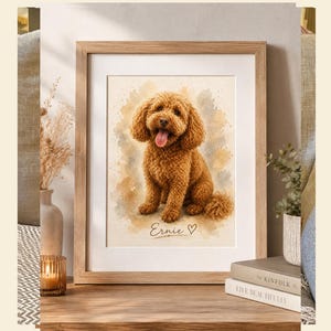 Può includere: Una stampa incorniciata in stile acquerello raffigurante un cane marrone dal pelo riccio seduto con la lingua di fuori. Il nome Ernie è scritto in corsivo sotto il cane, accompagnato da un piccolo simbolo a forma di cuore. Cornice in legno chiaro.
