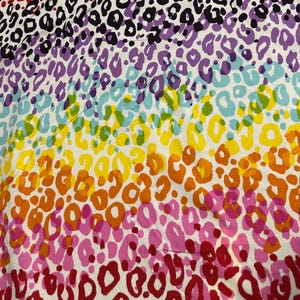 May include: A vibrant textile featuring a rainbow leopard print pattern. The design showcases a spectrum of colors, including red, pink, orange, yellow, green, blue, purple, and black spots, creating a bold and eye-catching visual.