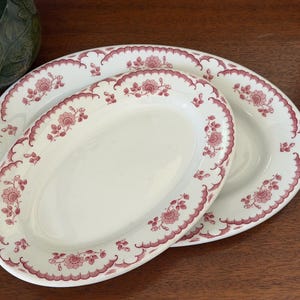 May include: Two oval ceramic platters featuring a white base with a decorative maroon floral pattern along the scalloped edges. The design consists of repeating flower motifs and leafy vines arranged in a border around the rim of each dish.