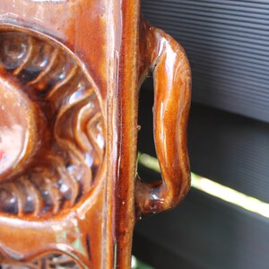Op de afbeelding: Een bruine keramische bakvorm met een handvat. De vorm heeft een decoratief ontwerp met reli&euml;fdetails.