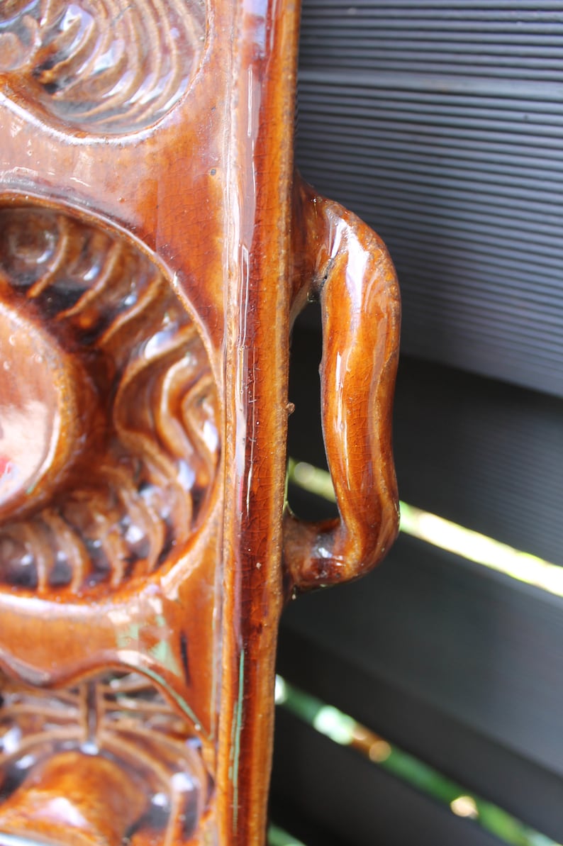 Op de afbeelding: Een bruine keramische bakvorm met een handvat. De vorm heeft een decoratief ontwerp met reli&euml;fdetails.