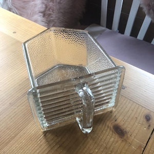 Peut inclure: Un récipient en verre transparent avec une surface texturée et une poignée. Le récipient a une forme rectangulaire avec un dessus arrondi.