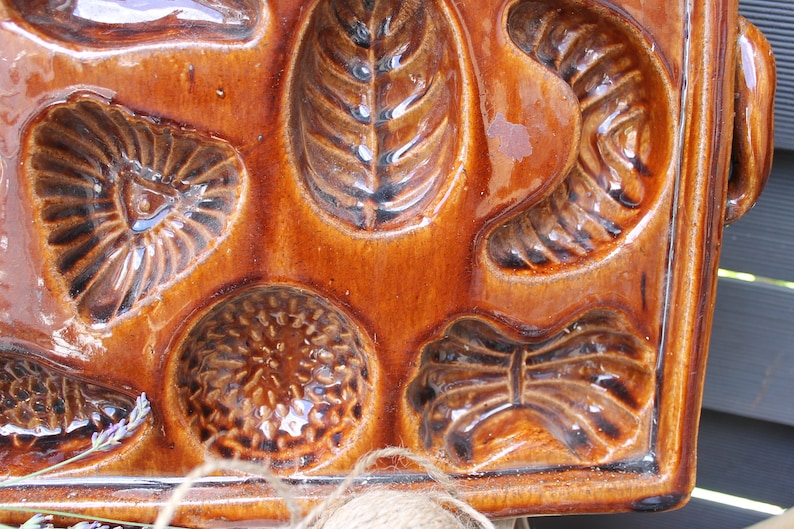 Op de afbeelding: Een vintage bruine keramische bakvorm met acht verschillende vormen. De vorm is geglazuurd en heeft een glanzende afwerking.
