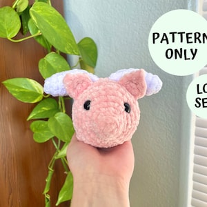 May include: A pink crocheted pig with purple ears and black eyes. The pig is being held in a hand. The text "PATTERN ONLY" and "LOW SEW!" is visible in the background.