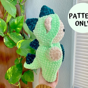 May include: Green and blue crocheted dinosaur plush toy. The toy is made with a soft, fuzzy yarn and has a cute, friendly expression.