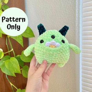 May include: A crochet pattern for a green, plush monster with black horns and a flower on its face. The pattern is available for download.
