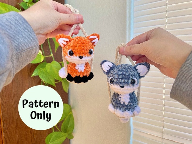 May include: A crochet pattern for making two amigurumi toys: a fox and a dog. The fox is orange and white, and the dog is gray and white. Both toys are hanging from a string.