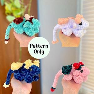 Könnte beinhalten: Vier gehäkelte Plüschdrachenspielzeuge in verschiedenen Farben: Türkis, Lavendel, Blau und Rosa. Jeder Drache hat einen langen Schwanz und kleine Flügel. Der Text "Pattern Only" ist in der Mitte des Bildes sichtbar.