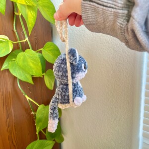 May include: A crocheted plush toy in the shape of a cat, with a blue and white color scheme. The cat is hanging from a white string.