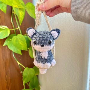 May include: A small crocheted plush toy in the shape of a dog, with blue and white fur, hanging from a cream-colored string.