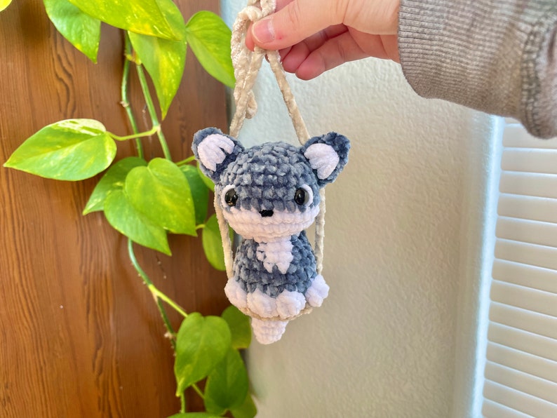 May include: A small crocheted plush toy in the shape of a dog, with blue and white fur, hanging from a cream-colored string.