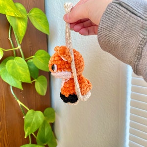May include: A crocheted orange fox with black eyes and a white nose hanging from a white string.
