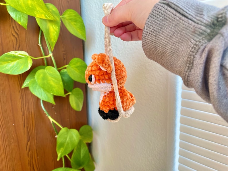 May include: A crocheted orange fox with black eyes and a white nose hanging from a white string.
