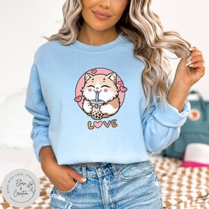 May include: Light blue cropped sweatshirt featuring a cartoon cat drinking bubble tea and the word "LOVE" with a pink heart in the middle.
