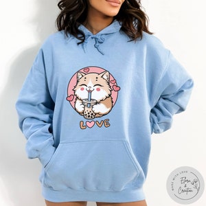 May include: Light blue hoodie featuring a cartoon cat drinking bubble tea and the word "LOVE" with a heart in the middle. The cat is surrounded by pink hearts.