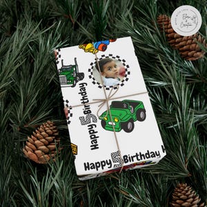 May include: A wrapped present with a white background, decorated with green trucks and a green jeep. The gift is tied with twine and has a circular photo of a child. The words "Happy 5th Birthday" are printed on the wrapping paper.