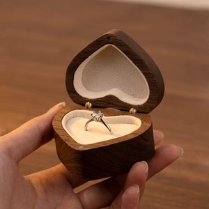 May include: A heart-shaped wooden ring box with a velvet interior. A silver ring with a single diamond is displayed inside the box.