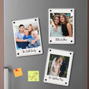 以下が含まれることがあります： 家族やカップルの写真が入った、透明なアクリル製のフォトマグネットが3つ。1つのマグネットには「The Smith Family」、別のマグネットには「Katie & Alice」、3つ目には「Our Wedding Day」と書かれています。付箋も2つ見えます。