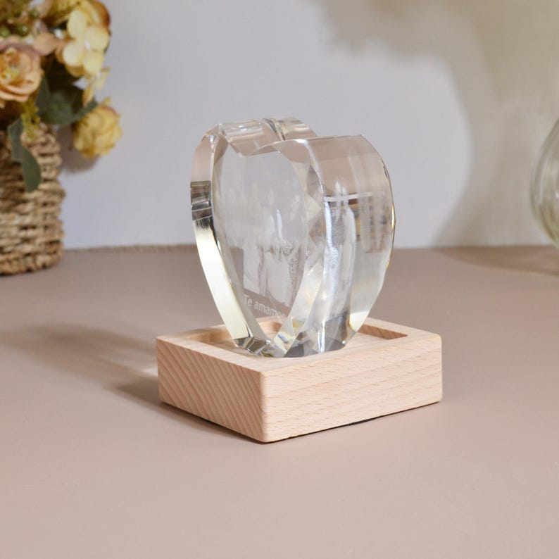 May include: A clear glass heart-shaped ornament with a photo inside, sitting on a wooden base. The photo is of a group of people and the text "Te amo" is visible.