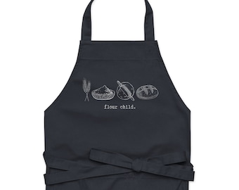 May include: A dark blue apron with a white graphic of wheat, flour, a rolling pin, and bread. The text "flour child." is printed below the graphic.