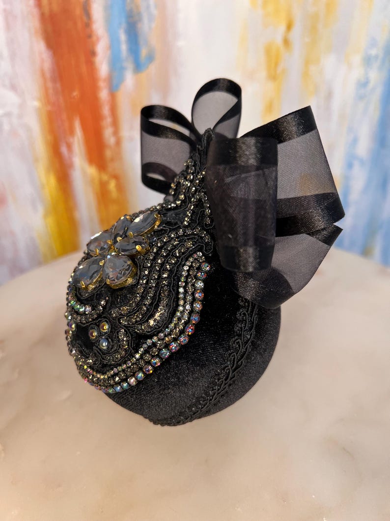 May include: A black velvet ornament with a black satin bow and iridescent rhinestones. The ornament is decorated with a floral design and is perfect for adding a touch of elegance to any holiday decor.