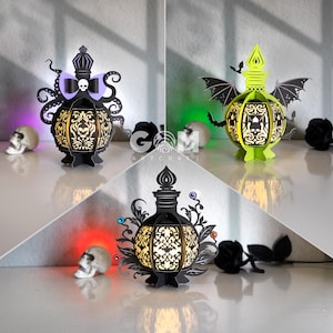 May include: Three decorative Halloween-themed paper lanterns. The lanterns are black with intricate cut-out designs, and each has a unique topper. One has tentacles and a bow, another has bat wings, and the third has floral accents. Each lantern is lit from within.