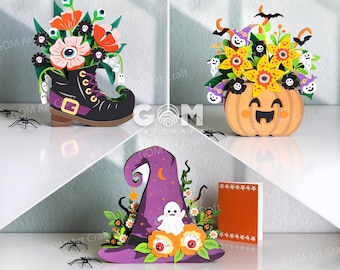 May include: Three decorative paper craft displays featuring Halloween themes. One is a black boot filled with flowers and eyeballs, one is a pumpkin with yellow flowers and ghosts, and one is a purple witch hat with a ghost and orange flowers.