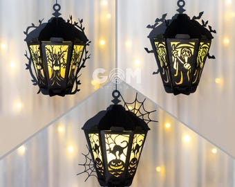 May include: Three black paper lanterns with intricate cut-out designs. The lanterns feature a spooky tree, a grim reaper, and a black cat with pumpkins. The lanterns are illuminated from within, casting a warm glow.