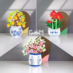 May include: Three-dimensional paper art featuring floral arrangements in decorative vases. The arrangements include a lemon tree, red amaryllis, and a flowering branch. The vases are white with blue floral patterns. The background is a neutral color.
