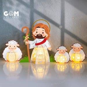 Può includere: Scena decorativa a tema religioso. Presenta una rappresentazione a cartoni animati di Gesù con un bastone e un'aureola, affiancato da tre pecore, ognuna con una lanterna luminosa. Lo sfondo è grigio, con il logo "GOM Art Craft".