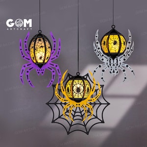 Puede incluir: Tres decoraciones de Halloween colgantes con forma de arañas con luces naranjas brillantes en su interior. Las arañas son moradas, blancas y negras con un diseño de telaraña. El texto "GOM ART CRAFT" es visible en el fondo.
