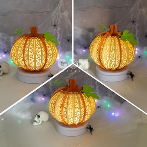 May include: A light-up pumpkin shaped lamp with intricate cutouts and a white base. The lamp is illuminated from within, casting a warm glow. The pumpkin is surrounded by a spiderweb and other Halloween decorations.