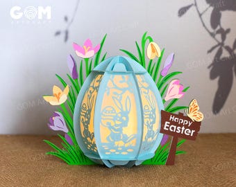 May include: A light blue papercraft Easter egg with a bunny rabbit design. The egg is surrounded by green grass and purple, pink, and yellow flowers. A sign reads "Happy Easter" with a butterfly.