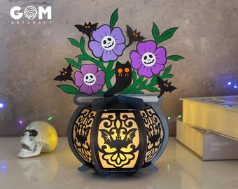 May include: A black cauldron with a light inside, decorated with bats and flowers. The flowers are purple with a skull design and the cauldron has a decorative design.