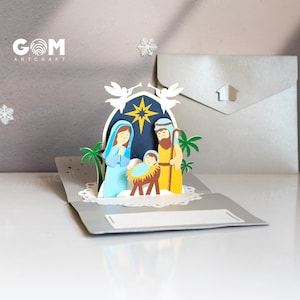 Pu&ograve; includere: Un biglietto di Natale pop-up con una scena della nativit&agrave; con Maria, Giuseppe e Ges&ugrave; bambino. Il biglietto &egrave; fatto di carta e ha uno schema di colori blu, giallo e marrone. Il biglietto include il testo "GOM Art Craft".