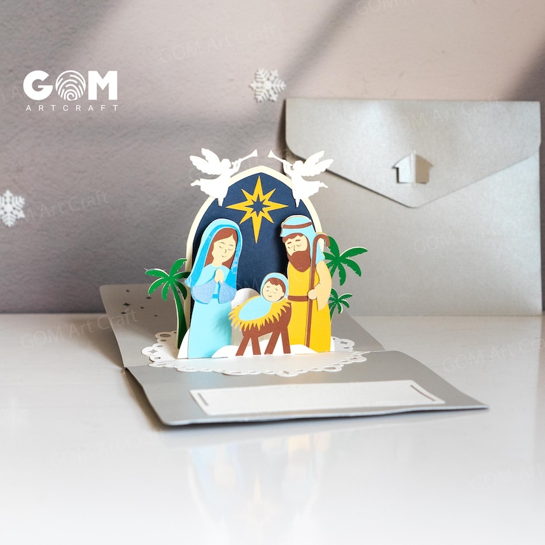 Pu&ograve; includere: Un biglietto di Natale pop-up con una scena della nativit&agrave; con Maria, Giuseppe e Ges&ugrave; bambino. Il biglietto &egrave; fatto di carta e ha uno schema di colori blu, giallo e marrone. Il biglietto include il testo "GOM Art Craft".