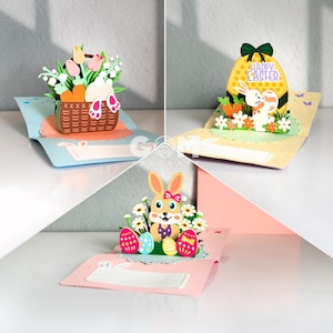 May include: Three Easter-themed pop-up greeting cards. One card features a basket of flowers with a bunny. Another shows a bunny and carrots with an egg that says "Happy Easter". The third card has a bunny with Easter eggs.