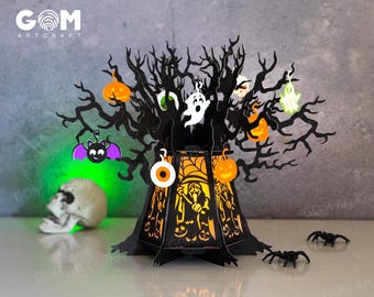 Pode incluir: Decoração de árvore de Halloween preta cortada a laser com abóboras laranja, fantasmas e um morcego. A árvore tem uma luz no interior e a base apresenta um design assustador. A caveira e as aranhas adicionam ao tema do Halloween. O texto "GOM ARTCRAFT" é visível.