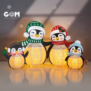 May include: Four penguin lanterns, each with a festive hat and scarf, illuminated from within. The lanterns are in various sizes and have a warm glow. The text "GOM Art Craft" is visible in the upper left corner.