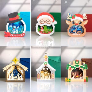 May include: A collection of Christmas-themed paper cut light boxes. Designs include a snowman, Santa Claus, a reindeer, a nativity scene, a church, and a fireplace, all with intricate layered details and festive colors.