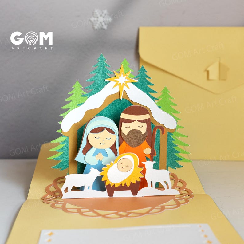 Pu&ograve; includere: Un biglietto di Natale pop-up con un presepe. Il biglietto raffigura Maria, Giuseppe e Ges&ugrave; bambino in una mangiatoia, con due pecore. La scena &egrave; ambientata in una stalla con alberi verdi e una stella. Il biglietto &egrave; giallo con il testo "GOM Art Craft".