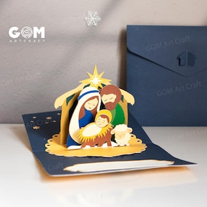 Pu&ograve; includere: Un biglietto di Natale pop-up con una scena della nativit&agrave; con Maria, Giuseppe e Ges&ugrave; bambino. Il biglietto &egrave; blu con una stella dorata e un piccolo agnello. Il biglietto &egrave; aperto, rivelando la scena ritagliata in carta 3D. Il biglietto ha il testo "GOM Art Craft".