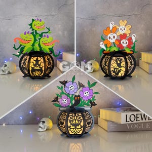May include: Three Halloween-themed light-up lanterns. The first lantern features a black cauldron with a witch inside and three green, carnivorous plants with red mouths. The second lantern features a black cauldron with a ghost inside and orange, yellow, and red flowers with skulls. The third lantern features a black cauldron with a cat inside and purple flowers with skulls.