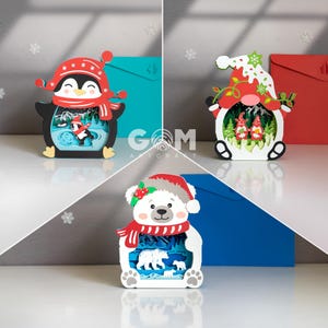 May include: Three-dimensional Christmas-themed layered art pieces. One features a penguin in a hat and scarf, another a gnome, and the last a polar bear. Each has a winter scene inside. The background includes blue and red envelopes.