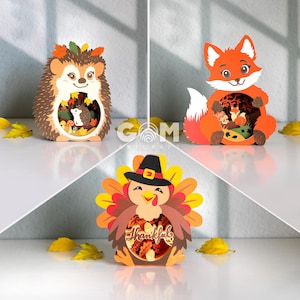 Peut inclure: Trois décorations en papier superposé représentant un hérisson avec des feuilles d'automne, un renard et une dinde portant un chapeau de pèlerin. La découpe de la dinde inclut le mot Thankful. Chaque figurine a une ouverture circulaire.