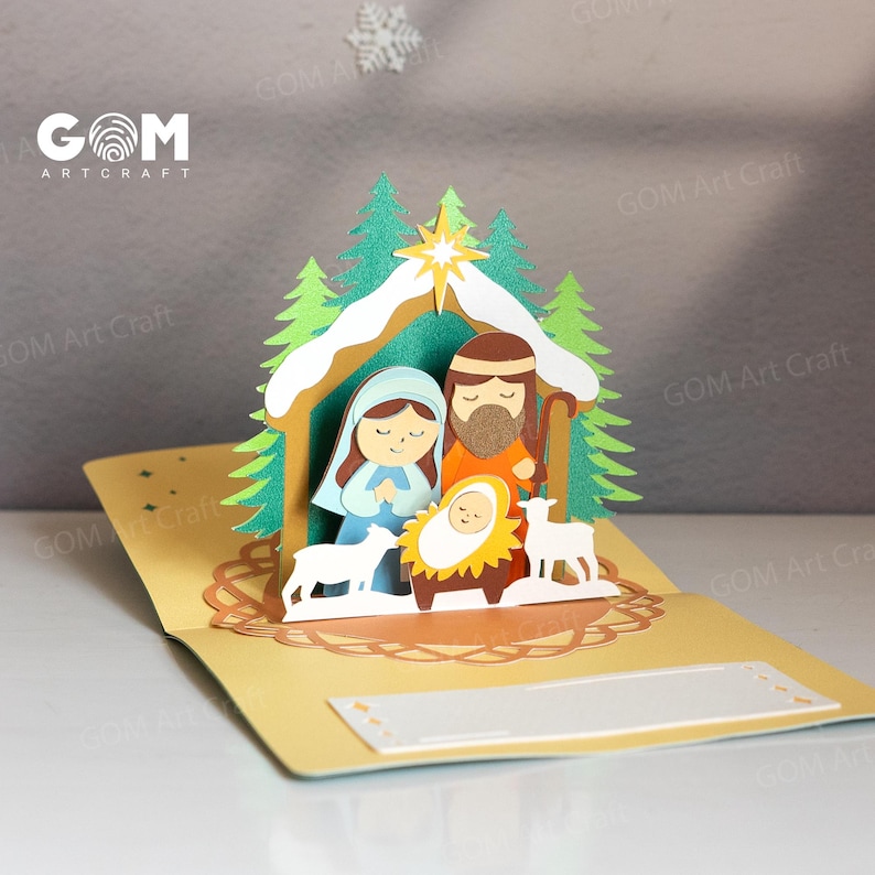 Pu&ograve; includere: Un biglietto di Natale pop-up con un presepe. Il biglietto raffigura Maria, Giuseppe e Ges&ugrave; bambino in una mangiatoia, con due agnelli. La scena &egrave; ambientata in una stalla con alberi verdi e una stella. Il biglietto &egrave; aperto e ha spazio per un messaggio.