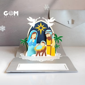 Pu&ograve; includere: Un biglietto di Natale pop-up con un presepe. Il biglietto raffigura Maria, Giuseppe e Ges&ugrave; bambino, con angeli e una stella sopra. Il biglietto &egrave; di carta e ha una combinazione di colori grigio e bianco.