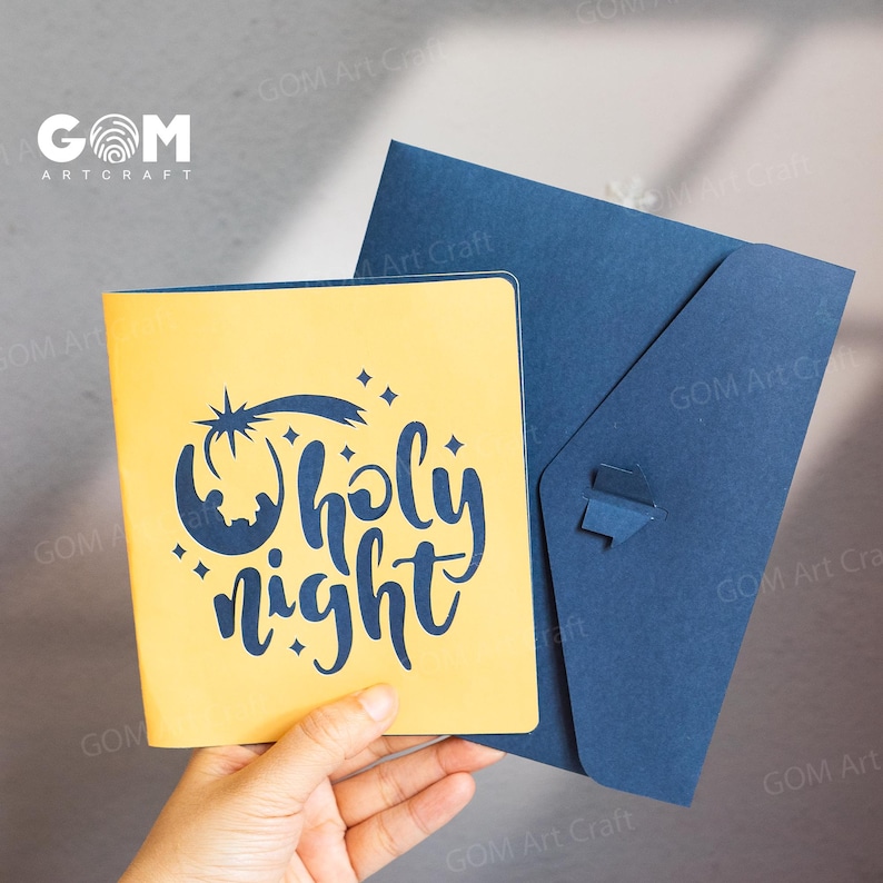 Pu&ograve; includere: Un biglietto di auguri giallo con la scritta "Holy Night" in corsivo, ornato da una stella e una luna crescente. Viene presentato con una busta blu scuro. Il biglietto &egrave; tenuto in mano.