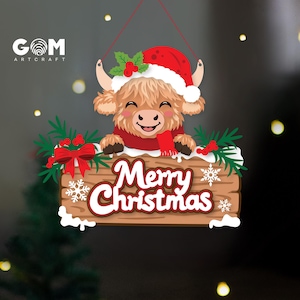 May include: A hanging Christmas ornament featuring a cartoon Highland cow wearing a red Santa hat and scarf, resting its hooves on a wooden sign that reads Merry Christmas in white letters, decorated with green pine branches, red berries, and snowflakes.