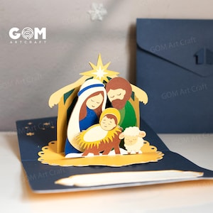 Pu&ograve; includere: Un biglietto di Natale pop-up con un presepe con Maria, Giuseppe e il bambino Ges&ugrave;. Il biglietto &egrave; realizzato in carta blu e gialla, con una stella e una pecorella. Il biglietto ha il testo "GOM Art Craft".